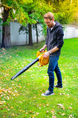 Man using a cordless leaf blower in a garden. Cleaning a lawn.
