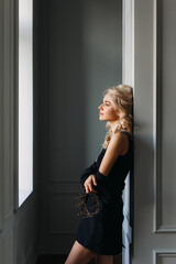 Elegant calm young blonde woman in black jacket, holding a crown in one hand.