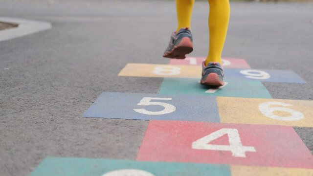 Little girl playing classics game painted on asphalt, jumping on colorful squares with numbers
