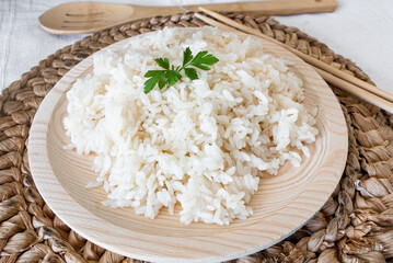 Cooked rice on a wooden plate, with some parsley leaves and a wooden chopsticks.