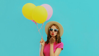 Portrait of beautiful young woman with bunch of colorful balloons blowing her lips sending sweet air kiss on a blue background