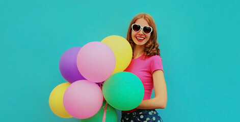 Portrait of happy smiling young woman with bunch of colorful balloons on a blue background
