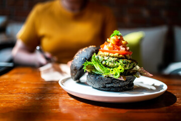 Broccoli quinoa charcoal burger topped with guacamole, mango salsa and fresh salad served on a white plate. Creative vegan meal for vegetarians.