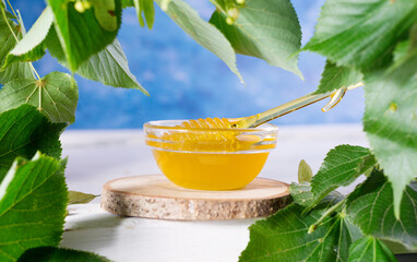Linden Honey in Jar and bowl with a honey dipper on a white wooden background. Defocused branch of linden in the foreground.