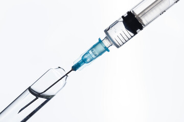 A syringe draws a vaccine from a medical bottle. On white.