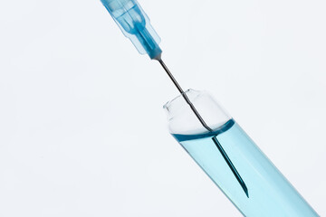 The syringe draws the blue vaccine from a medical bottle. On gray.