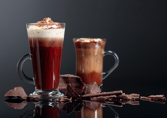 Hot chocolate with whipped cream and pieces of dark chocolate on a black reflective background.