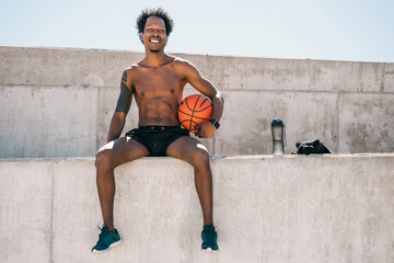 Afro athlete man holding a basketball ball outdoors.