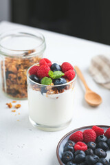 Yogurt with granola and berries in jar on white table, Vertical orientation
