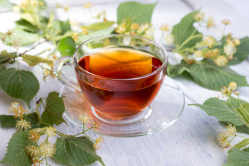 Glass cup of linden tea, and linden flowers on a white wooden table.