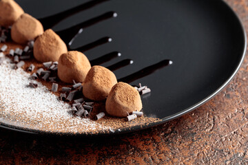 Chocolate truffles on a black plate with chocolate sauce.