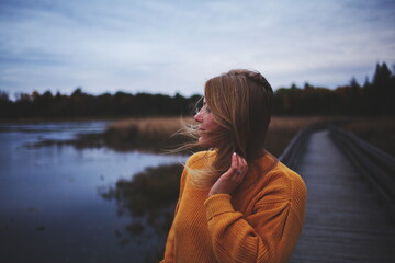 Woman in an orange sweater looking across the water at a local park in Ontario, Canada during the autumn season.
