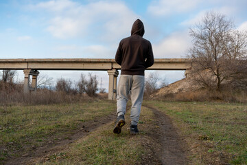 A man walks along a dirt road across which a bridge is built