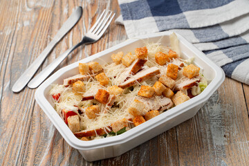 Food delivery: classic caesar salad with grated cheese and grilled chicken in a plastic box with no lid