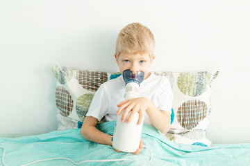 sick baby boy blonde doing inhalation in his bed at home, the concept of health and medicine