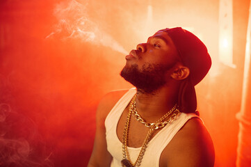 Stylish rapper exhales smoke in studio - obrazy, fototapety, plakaty