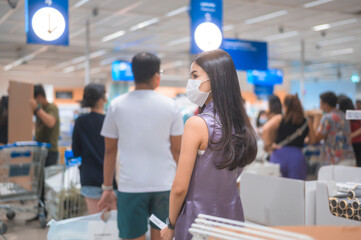 young woman wearing a surgical mask waiting in line near cashier counter in supermarket, covid-19...