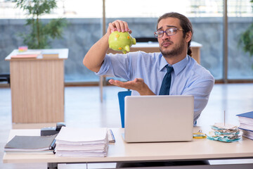 Fototapeta premium Young male accountant holding piggy bank at workplace