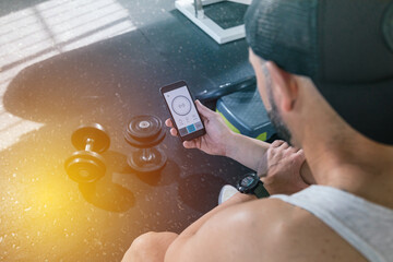A man with a smart phone in the gym. Looking at the screen of the smart phone. With dumbbells on the floor. health and wellness concept.