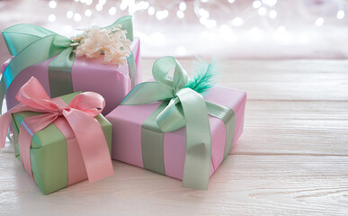 Three gift boxes with ribbons on a light background with a burning garland. Side view, with space to copy. The concept of festive backgrounds, March 8.