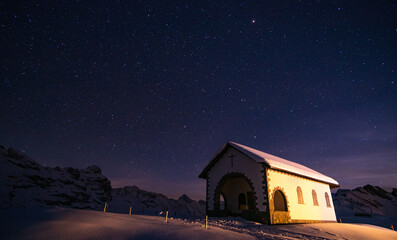 amazing winter night in the Swiss alps. bright stars, mountains, snow and a church in front in Melchsee-Frutt, Switzerland