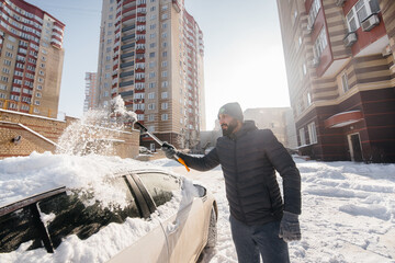 A young man cleans his car after a snowfall on a sunny, frosty day.
