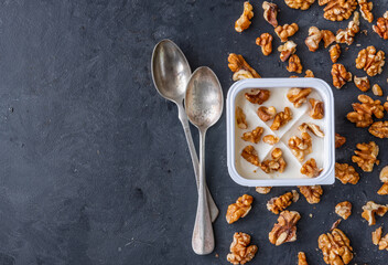White yogurt in plastic square cup with walnuts with spoons on gray background. Flat view.