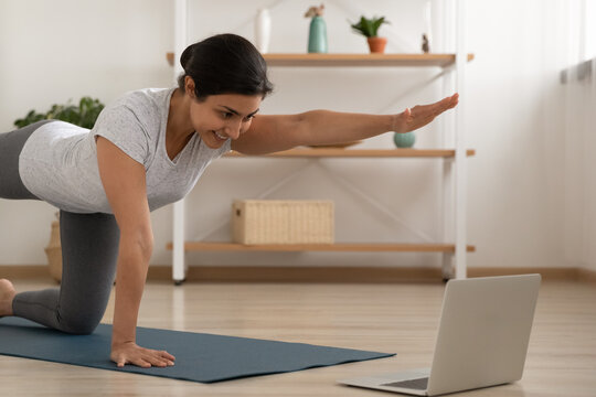 Young indian lady professional fitness trainer give yoga video lesson show stretching exercise before laptop webcam in conference mode. Motivated mixed race female take part in virtual sport training