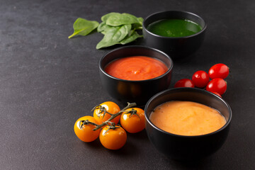 Plates of vegetarian soups: tomato, carrot, spinach. Dark photography.