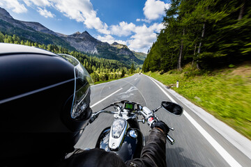 POV of motorbiker holding steering bar, riding in Alps in beautiful dramatic sky. Travel and freedom, outdoor activities