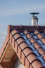 Naklejka premium Close-up of a traditional, most often used double pitched roof covered with tiles from terracotta in winter over the blue sky. Snow on the roof.