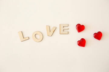 Wooden letters with the inscription of the word "Love" on a white background and next to a three small red hearts
