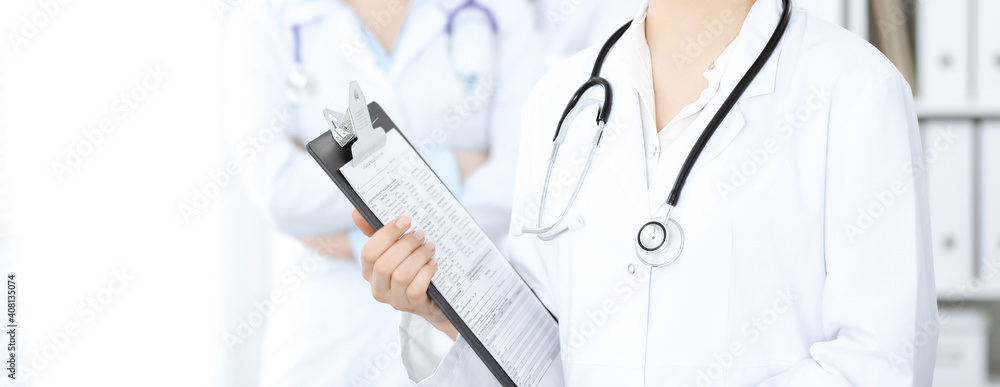 Wall mural unknown woman-doctor standing straight with clipboard of medication history record in clinic, close-