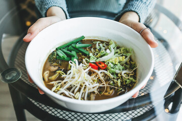 Close-up of a girl holding a plate with Ramen noodle soup in her hands. Asian traditional food.