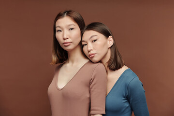 Gorgeous girl of Asian ethnicity keeping head on shoulder of her twin sister
