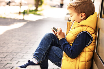 Side view of boy using cell phone outdoors.