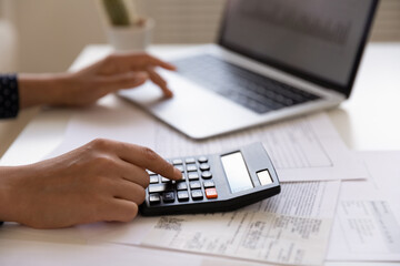Close up of young female electronic bank client using calculator in paperwork with accounts bills...