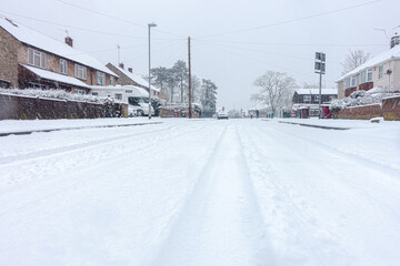 A residential road in Reading, Berkshire, UK is covered with snow. Car tracks lead into the distance.