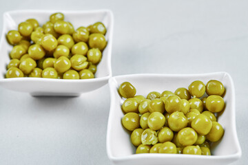 Two plates of boiled green peas on a grey background