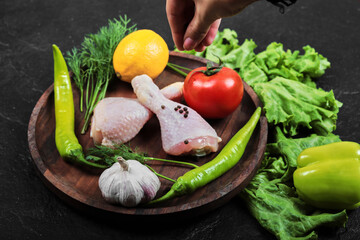 Woman hand holding a wooden plate of raw chicken legs with fresh vegetables