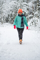 Fototapeta na wymiar A beautiful young woman in a winter wonderland enjoying the snow fashion walk wearing colourful jacket and red cap