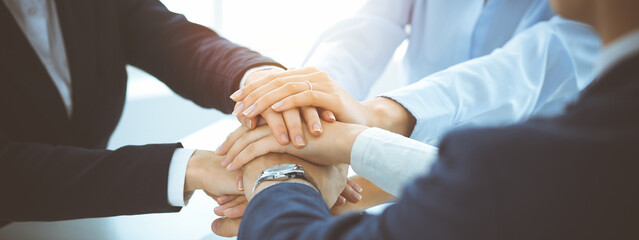 Business team showing unity with their hands together in sunny office. Group of people joining...