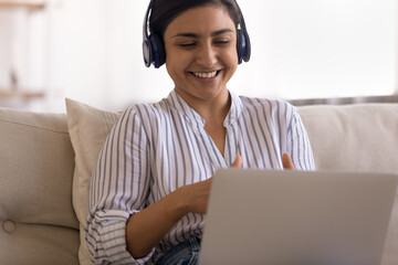 Smiling young indian businesswoman freelancer hold negotiations with customer using laptop headset. Skilled mixed race female sales manager working from home advertise product offer service to client - obrazy, fototapety, plakaty