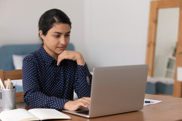 Pensive mixed race female university student on distant learning sit by laptop think on problem...