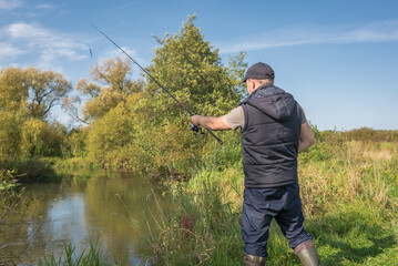 Man fishing with a rod on the river bank on a sunny day.