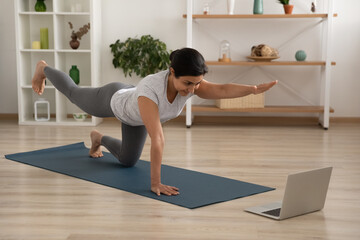 Active young female of indian ethnicity enjoy yoga at home practice static tiger asana. Mixed race...