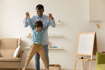 Overjoyed millennial indian dad and little kid boy having fun together play funny active game at...