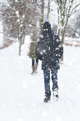 Fototapeta na wymiar two people walk on a snow-covered path in winter, a teenage boy and a girl, a snowstorm