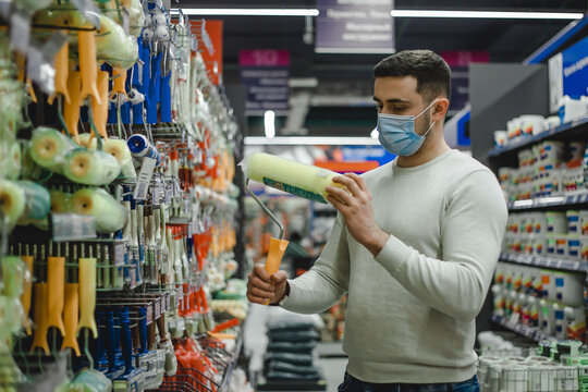 A buyer wearing medical mask chooses a paint roller in a hardware store.