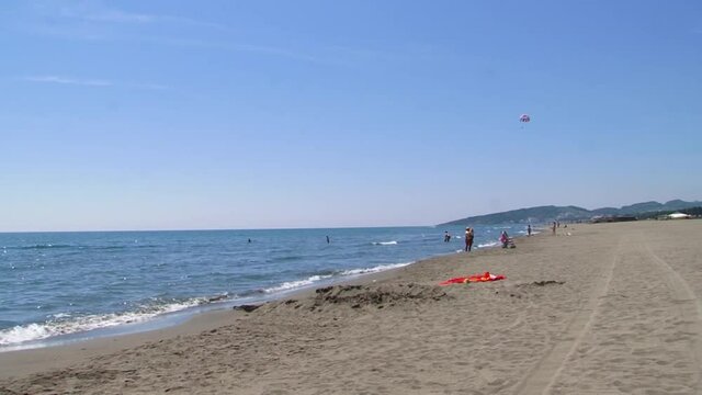 Ada Bojana sand beach with some people and kitesurfing. Small sea waves and bright blue sky.